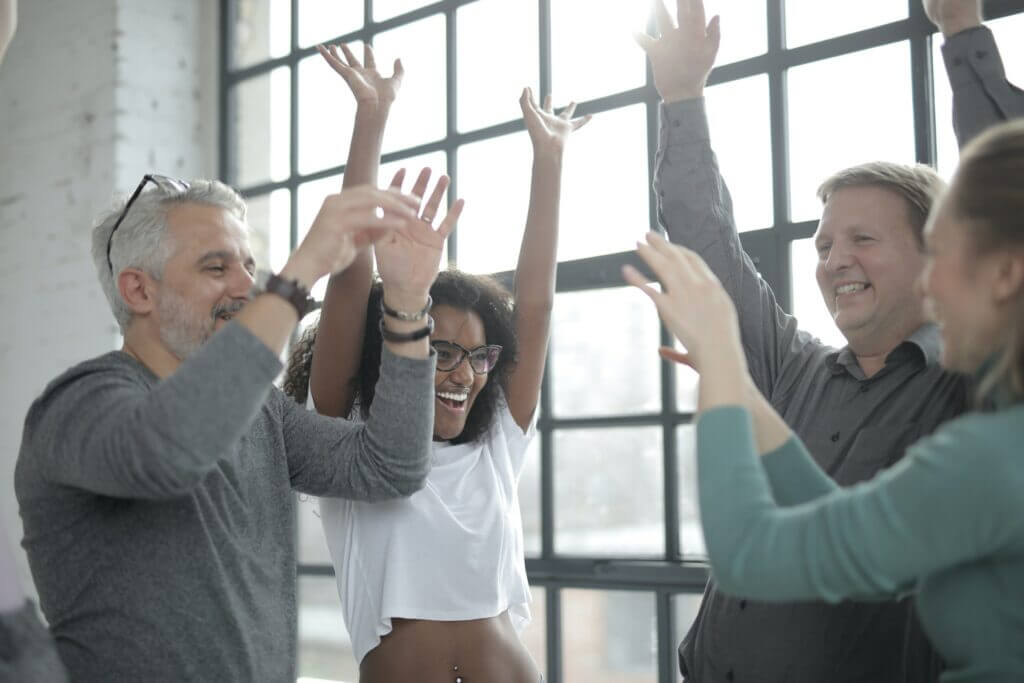 group of mixed race people in a circle with their hands in the air